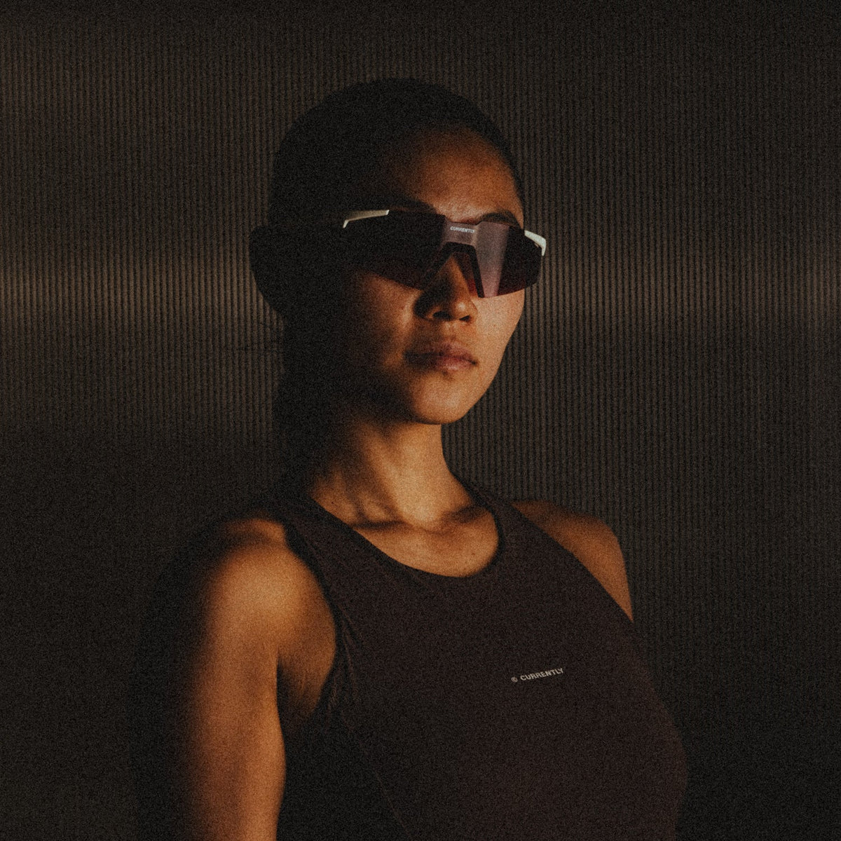 Currently Running™ x 100Percent® Collection - Featuring a girl runner wearing a Currently Running top and 100Percent A2 Sunglasses on a dark-warm moody background.