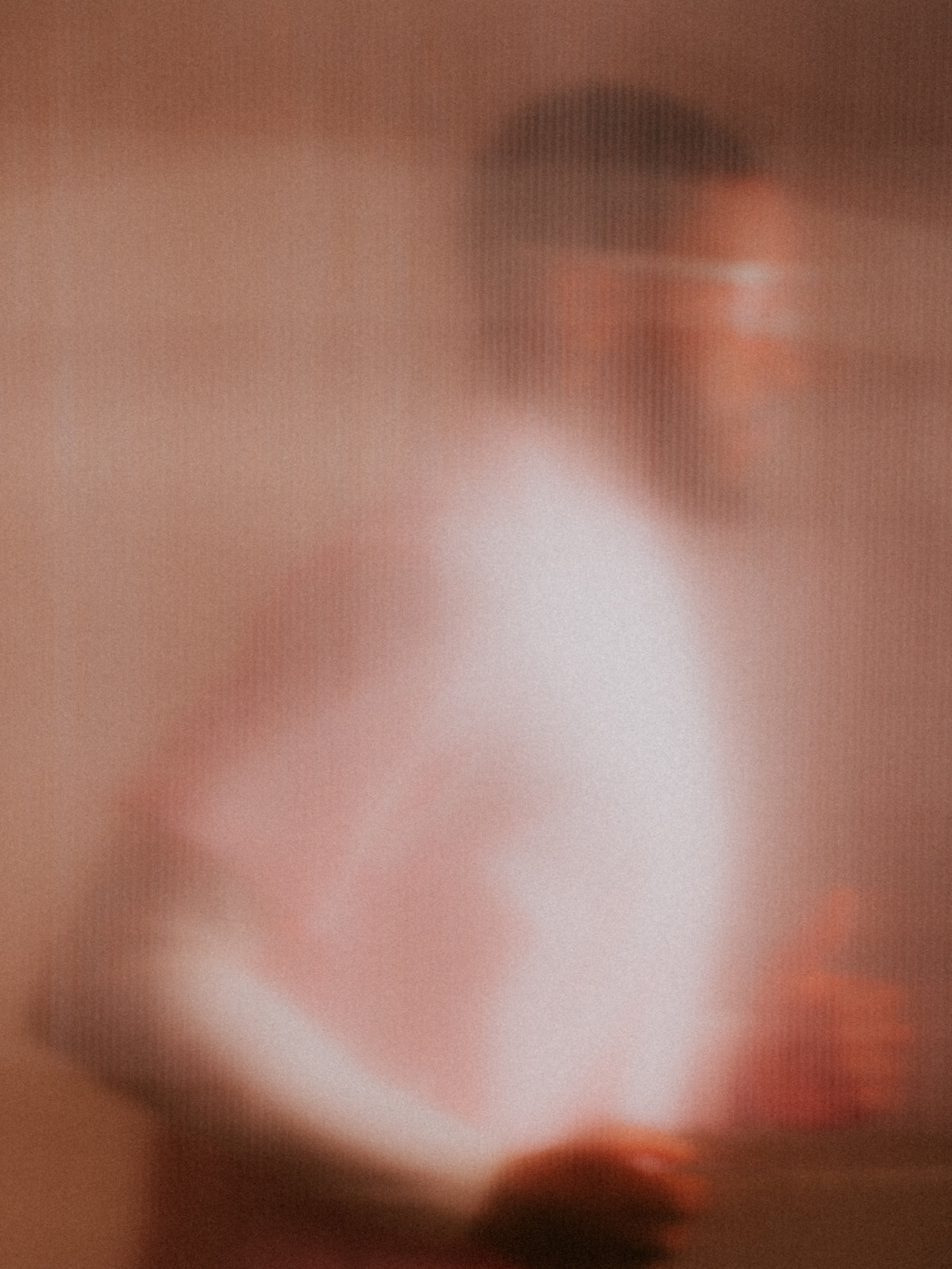 Currently Running™ x 100Percent® Collection. An abstract, heavily blurred photograph showing a soft pink and peach-toned figure against a matching warm background.