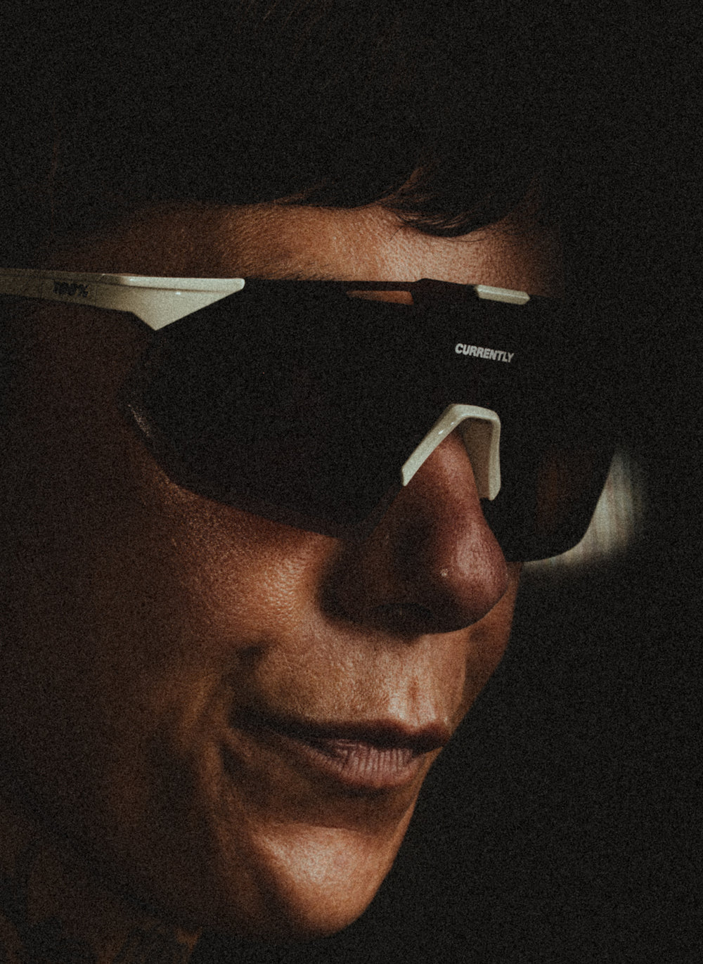 Currently Running™ x 100Percent® Collection - Featuring a girl runner wearing a Currently Running top and 100Percent Hypercraft® SQ Sunglasses on a dark-warm moody background.